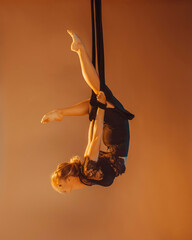 young girl in black costume is making aerial trick upside down on the beige background in photo studio in warm and cold lights, sport concept, free space