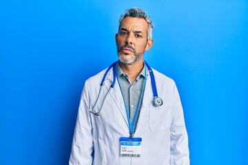 Middle age grey-haired man wearing doctor uniform and stethoscope relaxed with serious expression on face. simple and natural looking at the camera.