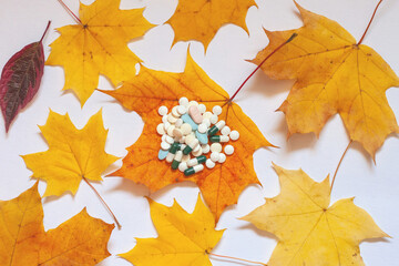 Flatley, yellow maple leaves on a white background, on a leaf in the middle are pills. Concept of increasing morbidity in autumn