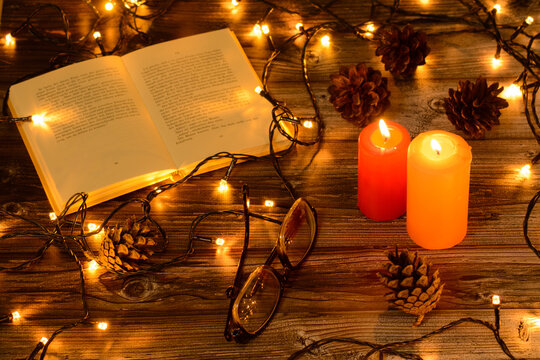 Christmas candles with boock and glasіes pine cones 
christmas lights on wooden background. Cristmas background 