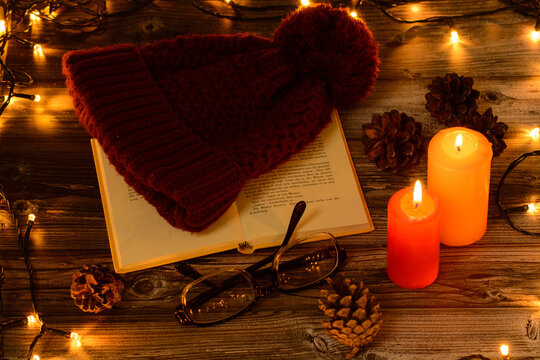Christmas candles with boock and glasіes pine cones 
christmas lights on wooden background. Cristmas background 