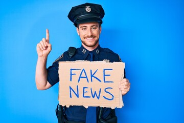 Young caucasian man wearing police uniform holding fake news banner surprised with an idea or question pointing finger with happy face, number one