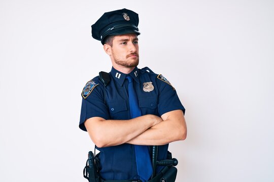 Young caucasian man wearing police uniform looking to the side with arms crossed convinced and confident