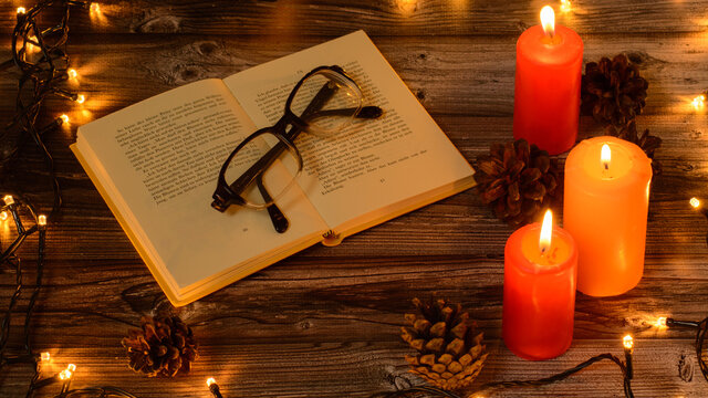 Christmas candles with boock and glasіes pine cones 
christmas lights on wooden background. Cristmas background 