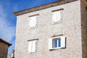 Old city. The facade of an old house made of light brick with white windows on a sunny day against the background of a light sky. Shutters on windows