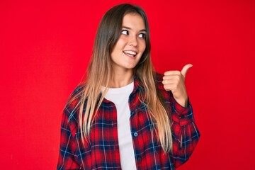 Beautiful caucasian woman wearing casual clothes smiling with happy face looking and pointing to the side with thumb up.