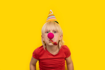 Boy in festive hat, whistle and red clown nose on yellow background. Children's party