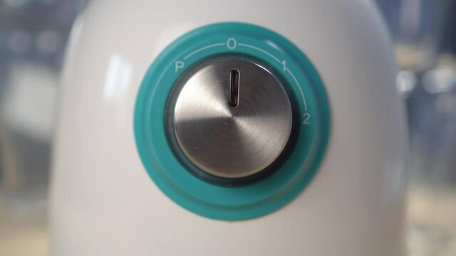 Turning off a kitchen mixer close-up. The hand rotates the metal button of the blender. Home electrical appliance with power adjustment. Selective focus