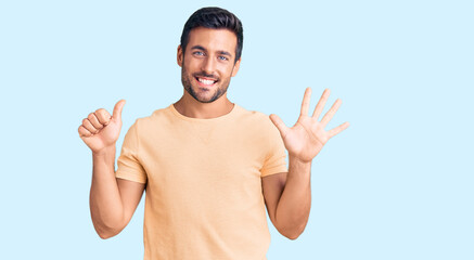 Naklejka premium Young hispanic man wearing casual clothes showing and pointing up with fingers number six while smiling confident and happy.