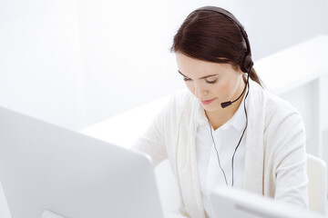 Call center. Casual dressed woman sitting and working in headset at customer service office. Business concept