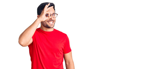 Young hispanic man wearing casual clothes and glasses smiling happy doing ok sign with hand on eye looking through fingers