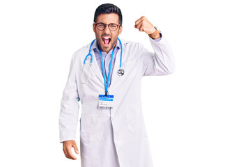 Young hispanic man wearing doctor uniform and stethoscope angry and mad raising fist frustrated and furious while shouting with anger. rage and aggressive concept.