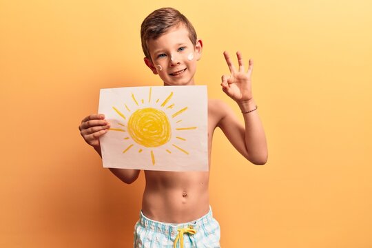 Cute blond kid wearing swimwear and summer hat doing ok sign with fingers, smiling friendly gesturing excellent symbol
