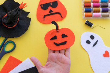 Halloween DIY pumpkin decoration concept: step by step making pumpkin, witch hat and ghost from felt paper on yellow background, woman hands