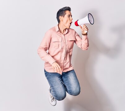Young beautiful caucasian woman screaming using megaphone. Jumping over isolated white background