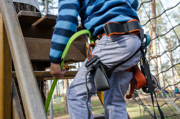 The boy climbs a rope park. Child's hands with safety harness.Close-up.