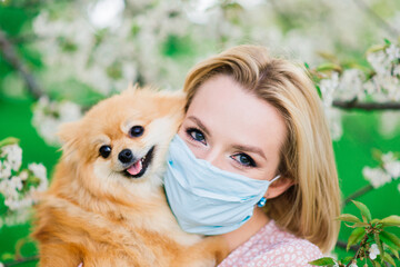 Young woman and red spitz with a medical mask on her face on nature on a spring day. Coronavirus