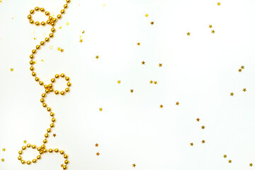 Garland of gold beads on a light background with star confetti. Flat lay style. Christmas or New Year concept. Place for text.