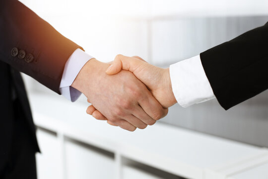 Businessman and woman shaking hands in sunny office, close-up. Concept of handshake as success symbol in business