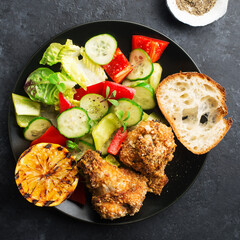 Appetizing crispy chicken wings breaded with bread crumbs with lettuce, sauce, lemon, microgreens in a plate on the table. Top view