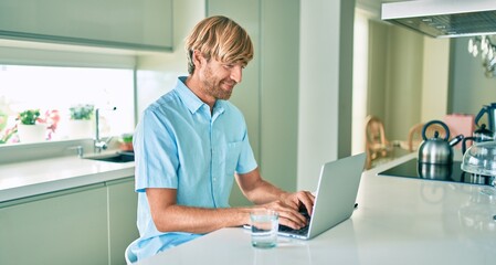 Young irish man smiling happy working using laptop sitting on the table at home.