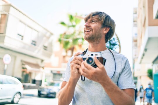 Young irish photographer man smiling happy using vintage camera at street of city.