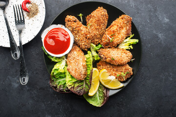Appetizing crispy chicken wings breaded with bread crumbs with lettuce, sauce, lemon, microgreens in a plate on the table. Top view