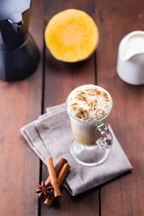 Pumpkin latte, milk jug and a piece of pumpkin. Pumpkin latte with whipped cream and spices on a wooden boards. Hot autumn coffee drink on a linen napkin