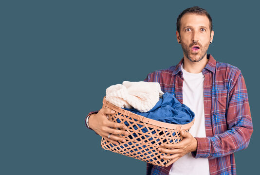 Young handsome man holding laundry basket scared and amazed with open mouth for surprise, disbelief face