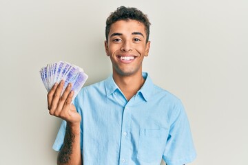 Young handsome african american man holding 20 swedish krona banknotes looking positive and happy standing and smiling with a confident smile showing teeth