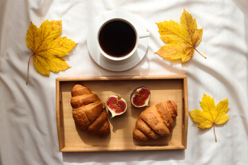 Autumn cozy lifestyle blog's flat lay with morning coffee, croissants, figs on a wooden tray and maple leaves. Top view