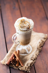 Pumpkin spice latte in a glass mug. Pumpkin latte with whipped cream and spices on a wooden background. Hot autumn coffee drink on a burlap