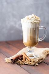 Pumpkin spice latte in a glass mug. Pumpkin latte with whipped cream and spices on a wooden background. Hot autumn coffee drink on a burlap