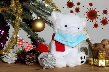 white teddy bear under christmas tree in pandemic COVID-19 with medical mask