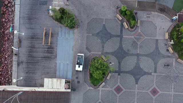 Street sweeper Brush Car cleaning a coastline resort promenade at sunrise, Aerial view.