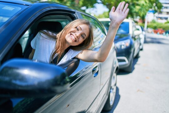 Young beautiful blonde woman smiling happy sitting at the car with hand out and cheerful expression