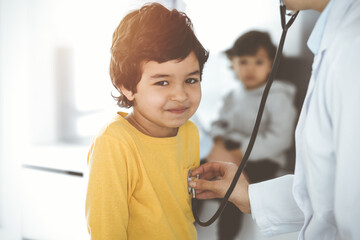 Woman-doctor examining a child patient by stethoscope in sunny clinik. Cute arab boy at physician appointment