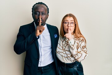 Young interracial couple wearing business and elegant clothes asking to be quiet with finger on lips. silence and secret concept.