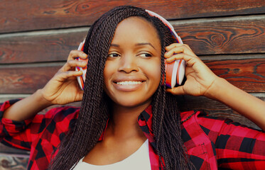 Portrait of happy young smiling african woman in wireless headphones over city background