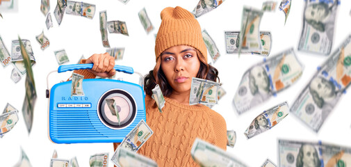 Young beautiful mixed race woman holding vintage radio thinking attitude and sober expression...