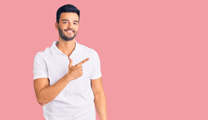 Young handsome hispanic man wearing casual clothes cheerful with a smile on face pointing with hand and finger up to the side with happy and natural expression
