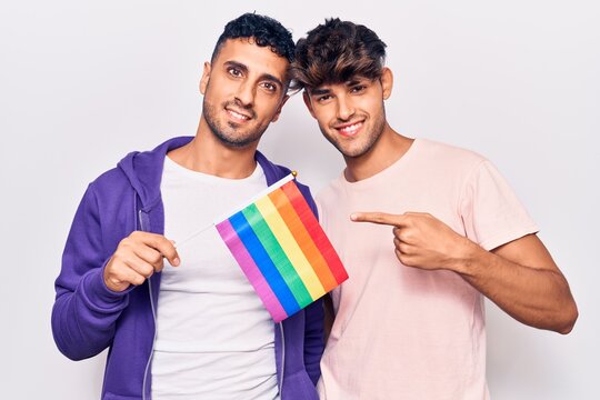 Young gay couple holding rainbow lgbtq flag smiling happy pointing with hand and finger