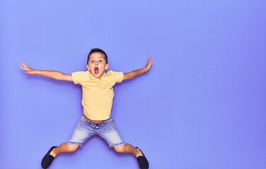 Obraz premium Adorable kid wearing casual clothes jumping over isolated purple background