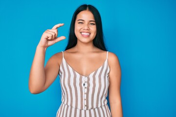 Young beautiful asian girl wearing casual clothes smiling and confident gesturing with hand doing small size sign with fingers looking and the camera. measure concept.