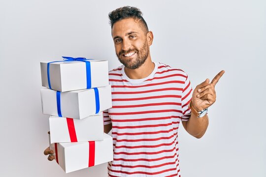 Handsome man with beard hodling with presents smiling happy pointing with hand and finger to the side