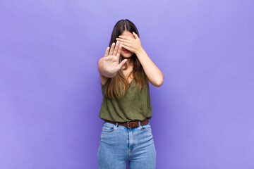 youn pretty woman covering face with hand and putting other hand up front to stop camera, refusing...