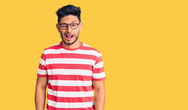 Handsome latin american young man wearing casual clothes and glasses winking looking at the camera with sexy expression, cheerful and happy face.
