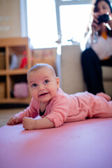 Mom Films Smiling Baby Girl Lying Down on a Pink Rug