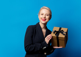 Style blonde in black jacket with gift box on blue background