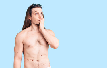 Fototapeta premium Young adult man with long hair wearing swimwear shirtless looking stressed and nervous with hands on mouth biting nails. anxiety problem.